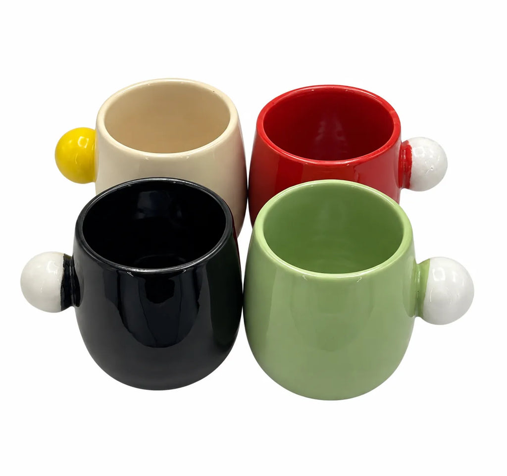 Four ceramic cups arranged in a 2x2 grid on a white background, each with a rounded body and a spherical handle on the side. The cups are in cream, red, black, and light green, with matching yellow, white, black, and white accents on the handles.