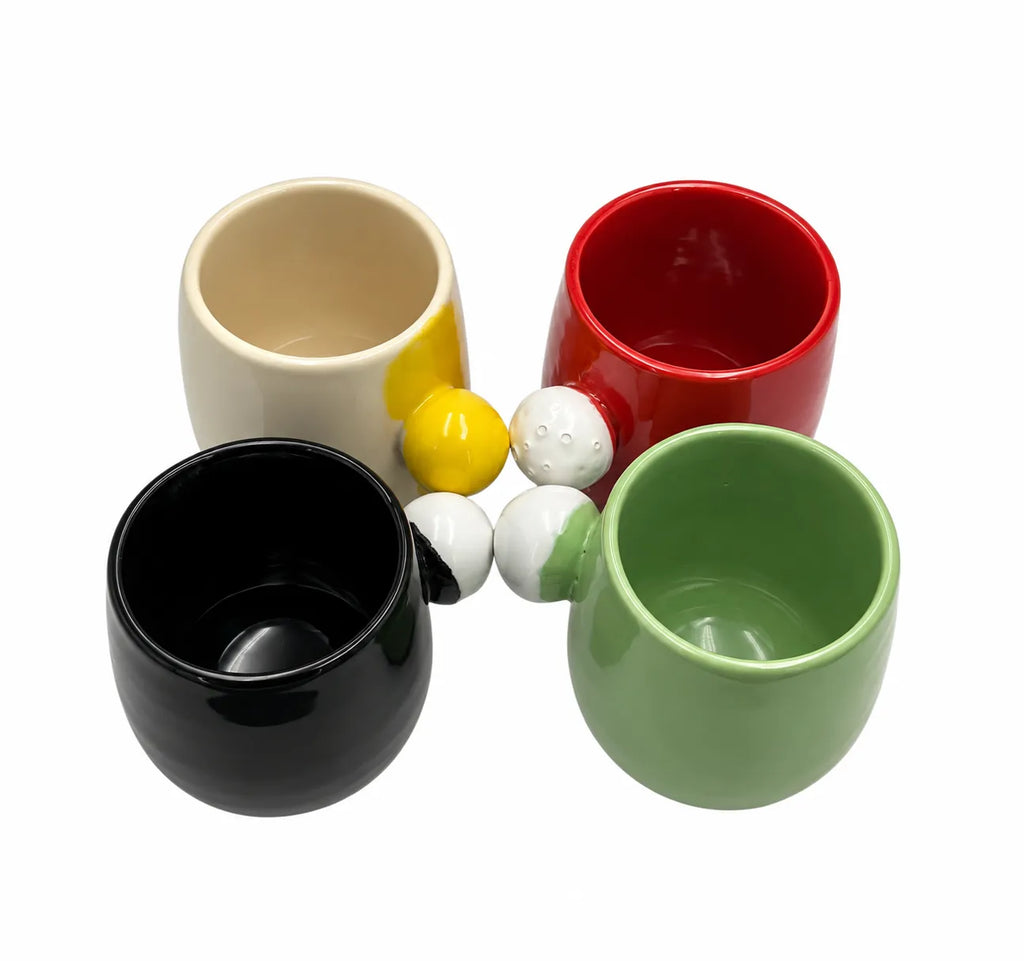 Four ceramic cups in black, cream, red, and green, arranged with small decorative golf balls on a plain white background.