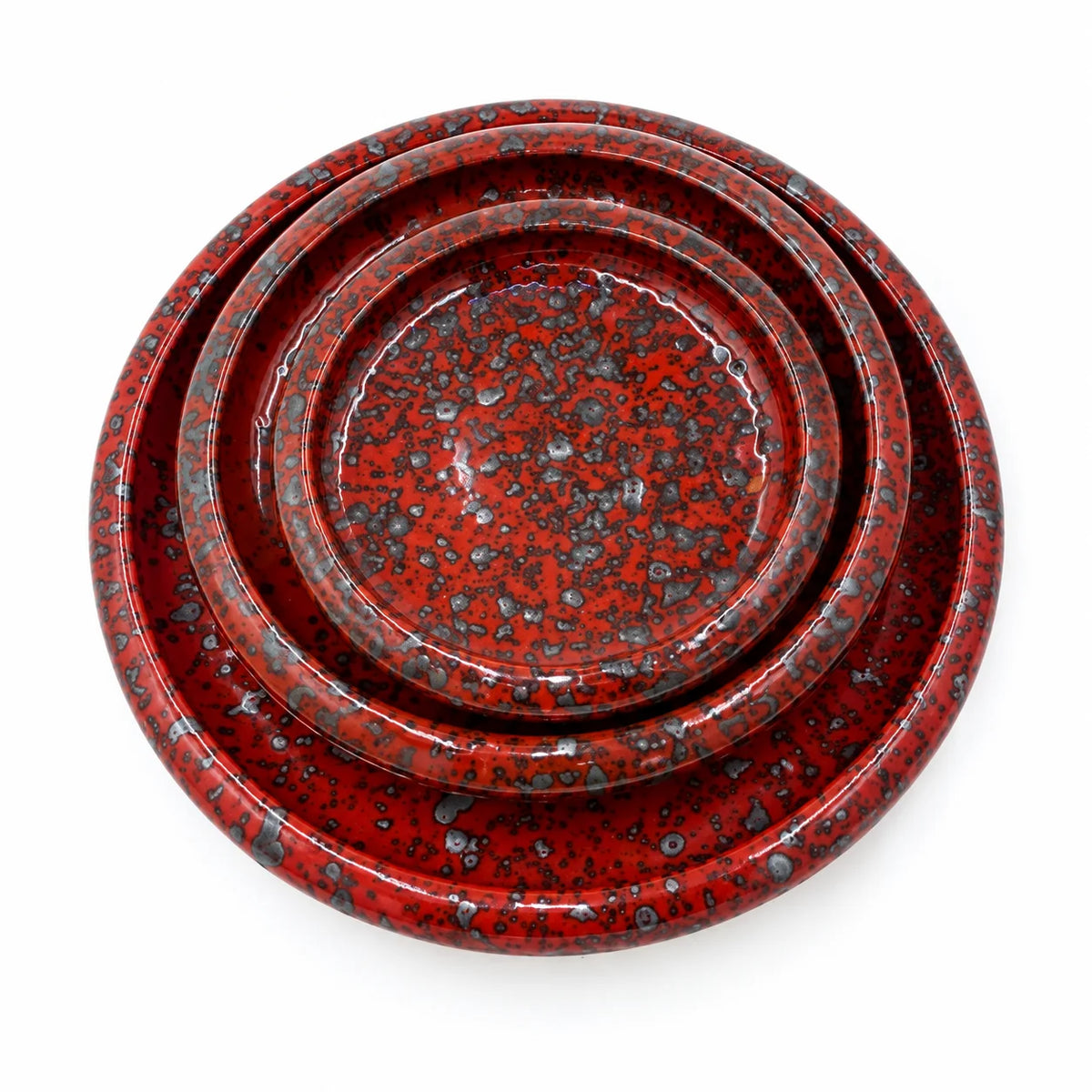 A set of nested round ceramic plates with a glossy red glaze and black speckled pattern, photographed from directly above on a white background.