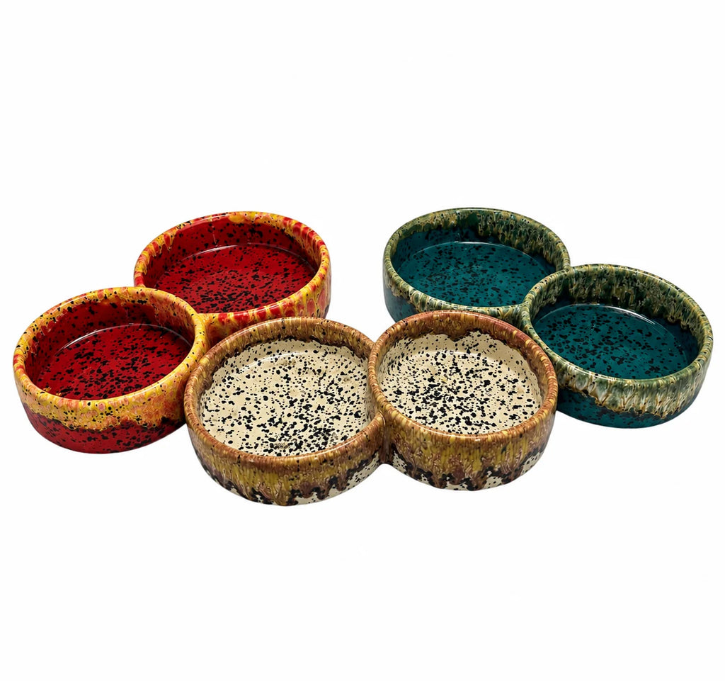 Five ceramic pet food bowls with colorful speckled glazes in red, teal, beige, and brown, arranged on a plain white background.