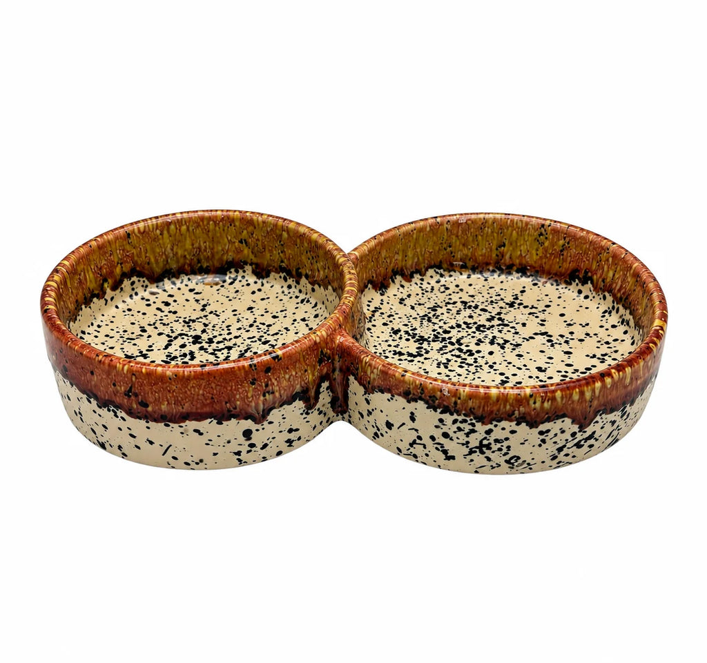 A two-compartment ceramic dish with a speckled glaze in cream, brown, and black, shown on a plain white background.