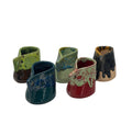 Five small ceramic bud vases with unique glazes and drippy finishes, displayed on a clean white background. The vases feature a variety of colors including green, blue, red, black, and brown.